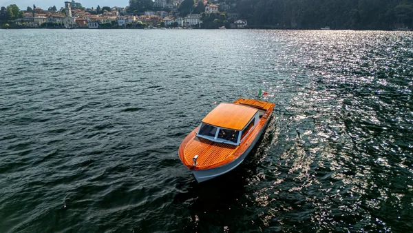 Barca classica in legno che arriva davanti a un borgo sul lago con il suo campanile
