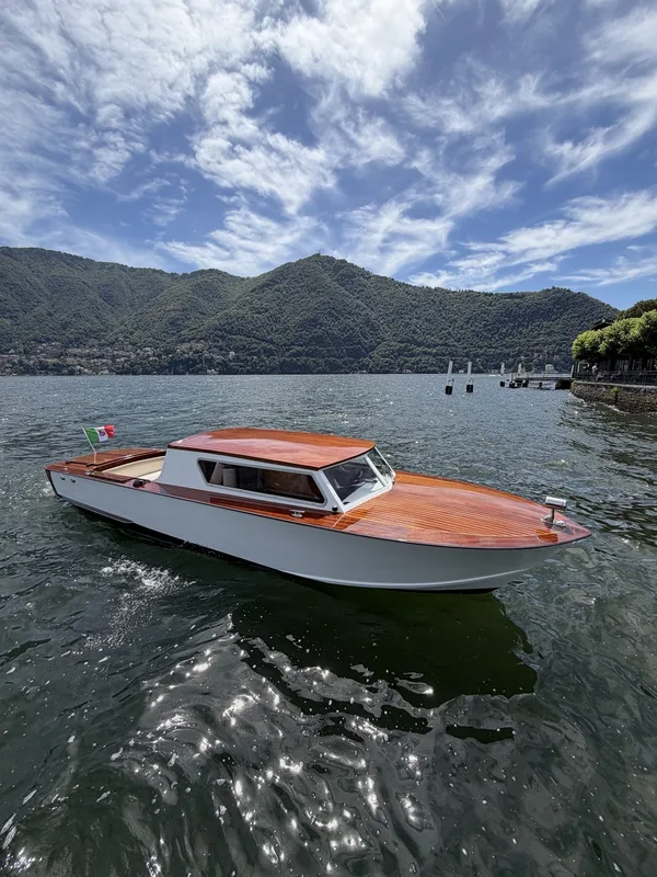 Una delle nostre barche con coperta in legno, scafo chiaro e cabina chiusa, ormeggiata sul Lago di Como