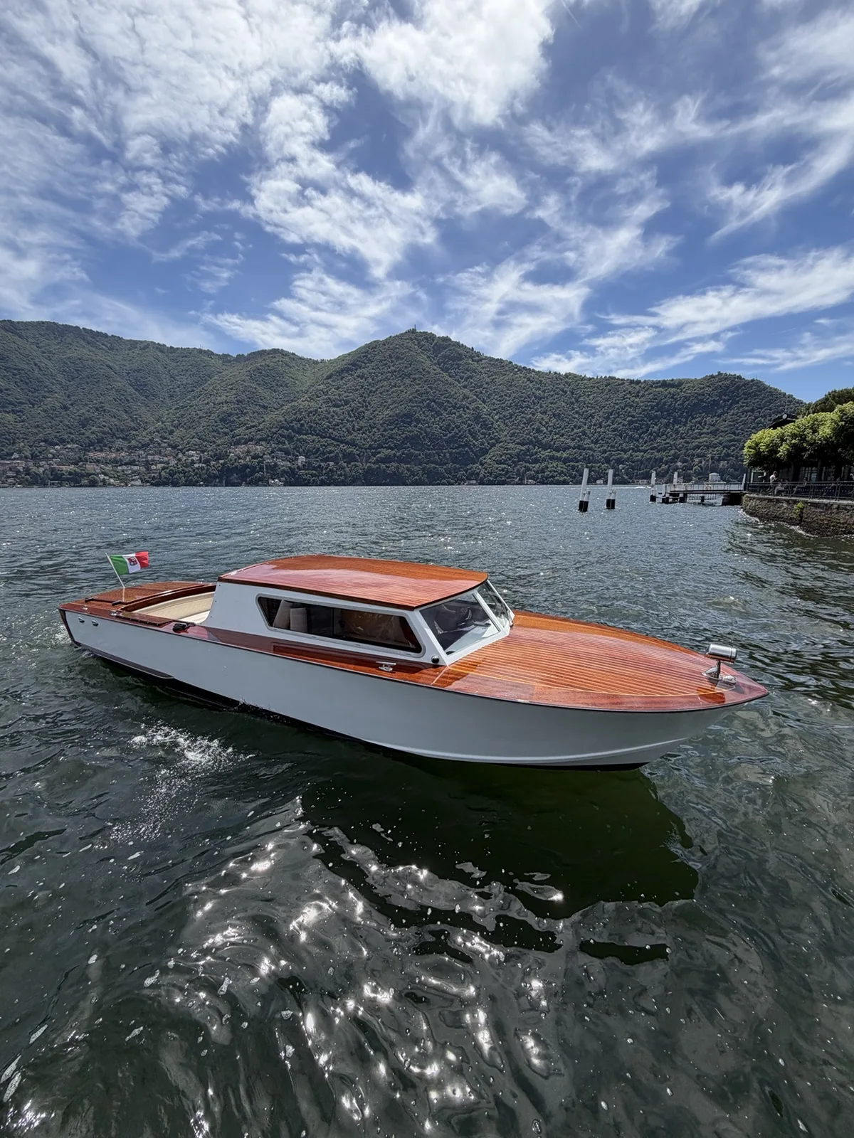 Una delle nostre barche con coperta in legno, scafo chiaro e cabina chiusa, ormeggiata sul Lago di Como