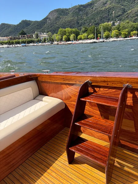 Divanetto in pelle avorio e scaletta in mogano a bordo, con la riva di Como alle spalle