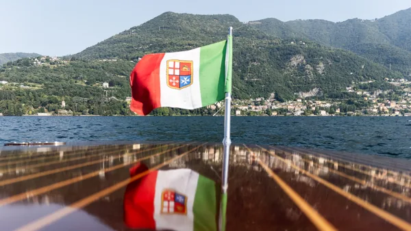Bandiera navale italiana riflessa sul ponte in mogano lucido, con il Lago di Como sullo sfondo