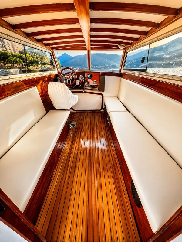 Dentro la cabina chiusa: panche color avorio, pavimento e soffitto in legno lucido e posto di guida con vista su lago e montagne